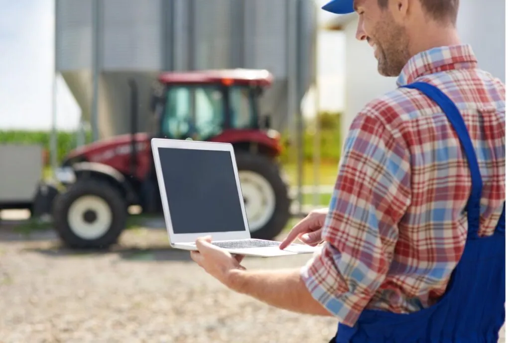 Farmer using a laptop near a red tractor