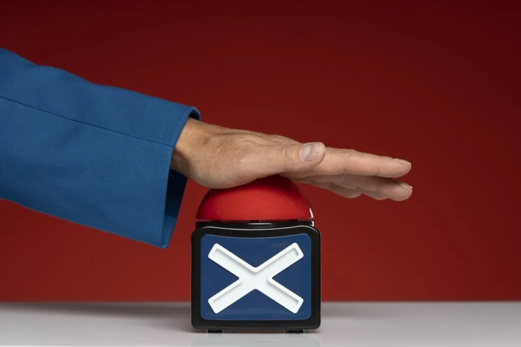 Hand pressing a red buzzer with an X