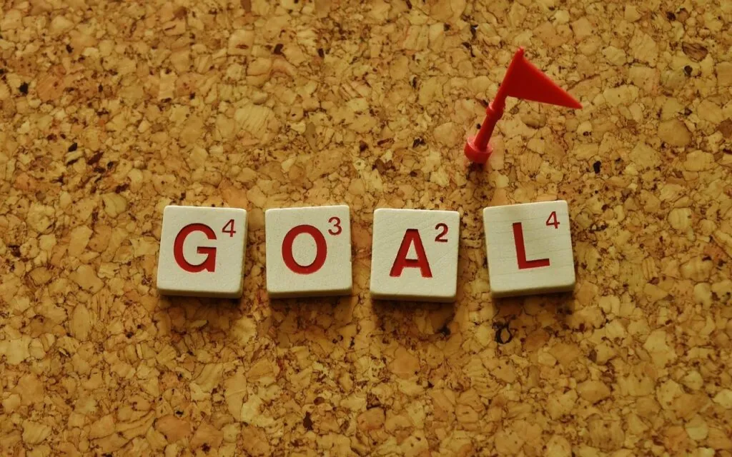 Scrabble tiles spelling "goal" with red flag