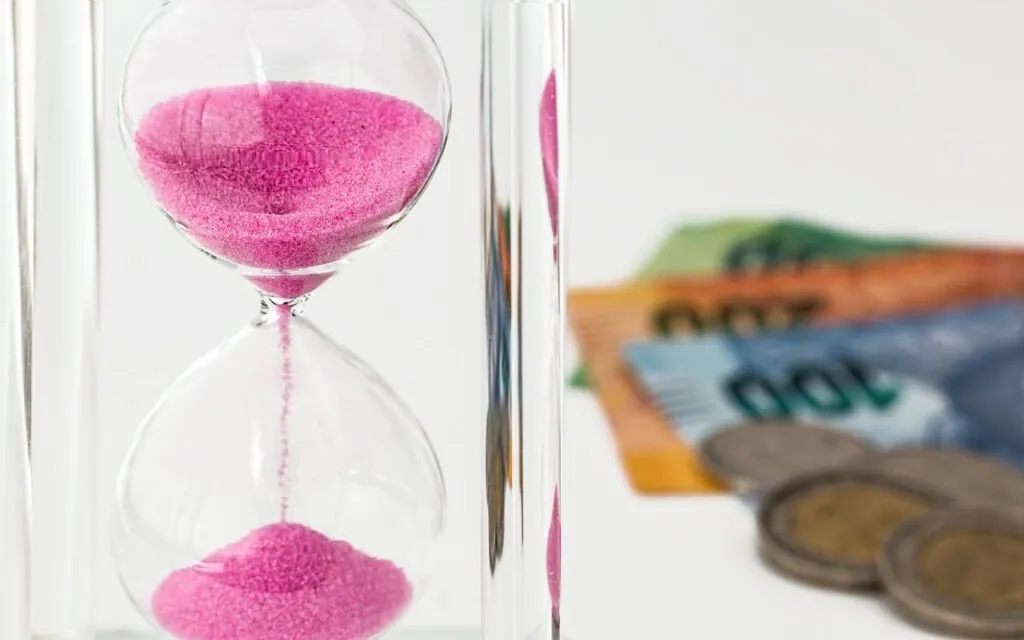Hourglass with pink sand and blurred currency