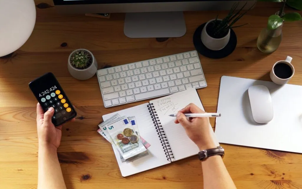 Person calculating expenses with smartphone notebook and money