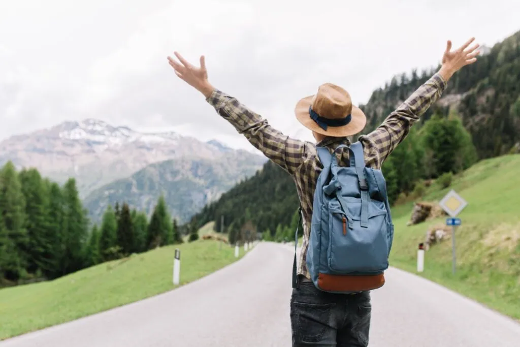Traveler with arms raised on mountain road