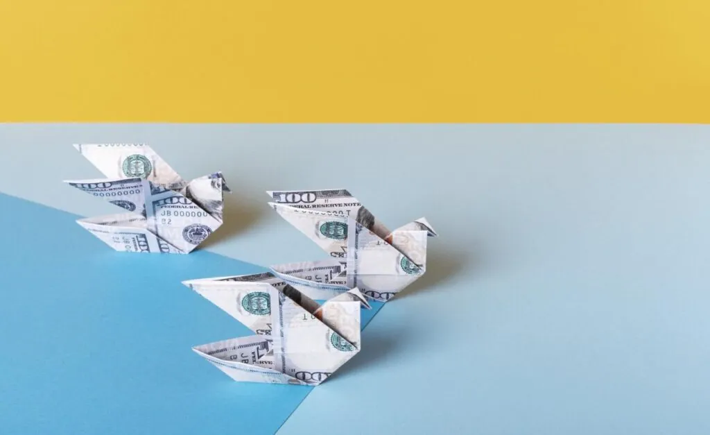 Origami birds made of dollar bills on colored background