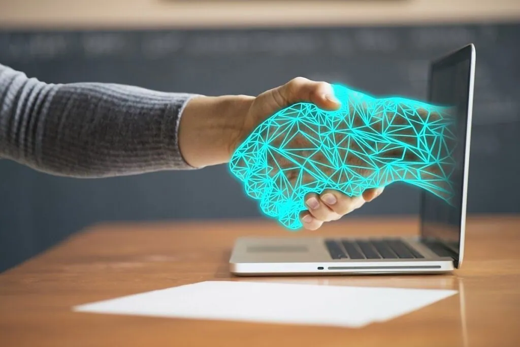 Person shaking a digital hand through laptop