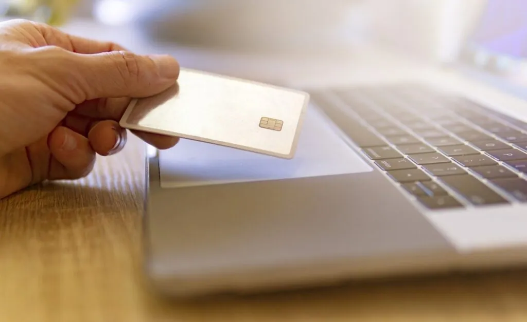 Hand holding a credit card near a laptop