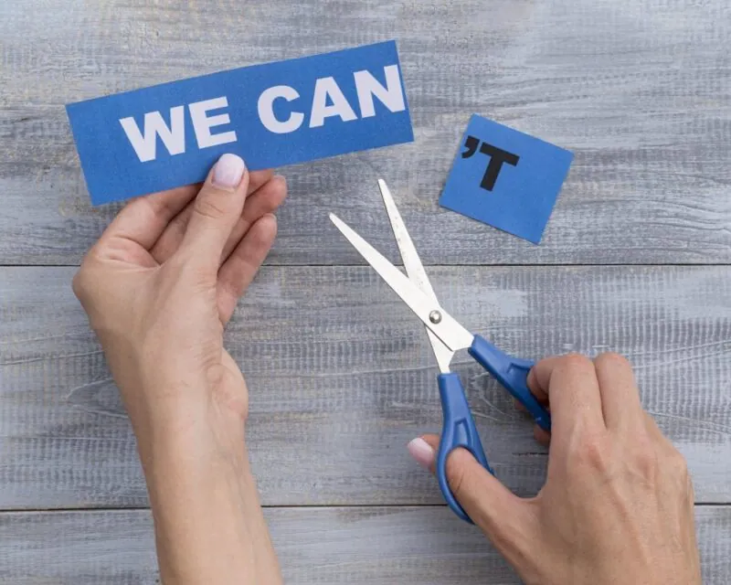 Hands cutting the letter T from WE CAN'T