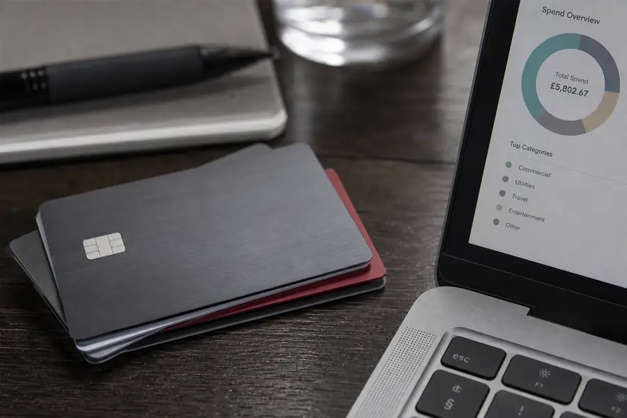 Of corporate cards laid on a desk beside a spend dashboard on a laptop, shallow depth of field, realistic photo