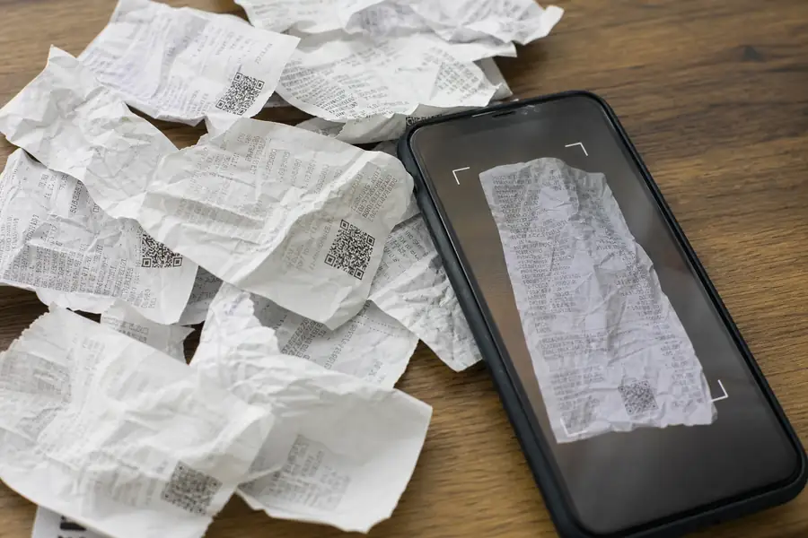 Crumpled paper receipts scattered next to a smartphone scanning one, realistic photo