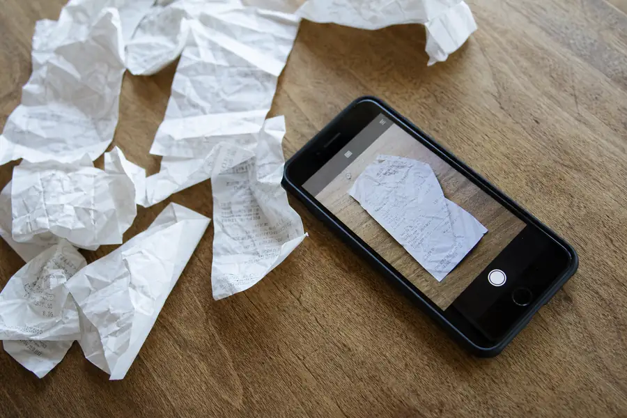 Crumpled paper receipts scattered next to a smartphone scanning one