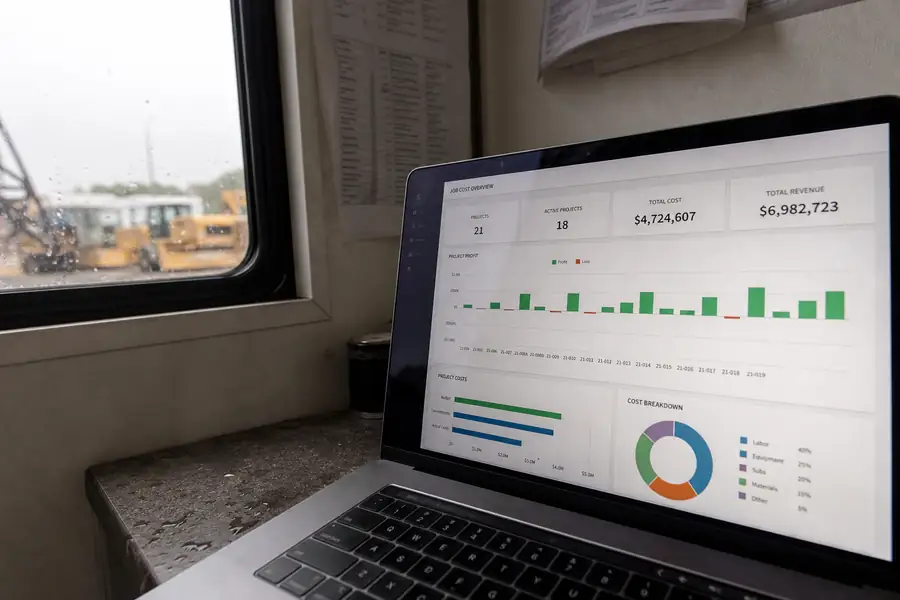 Of job cost dashboard with project profit bars on a laptop at a job site trailer, shallow depth of field, realistic photo