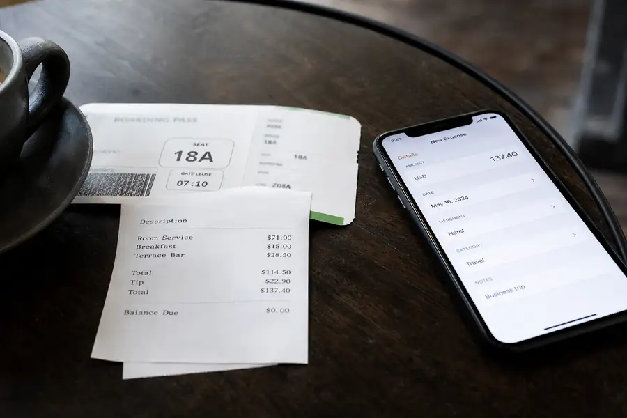 Boarding pass, hotel receipt and phone with an expense app on a cafe table
