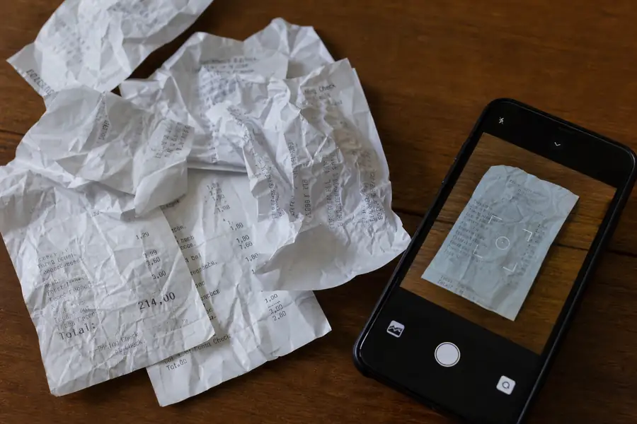 Crumpled paper receipts scattered next to a smartphone scanning one, realistic photo